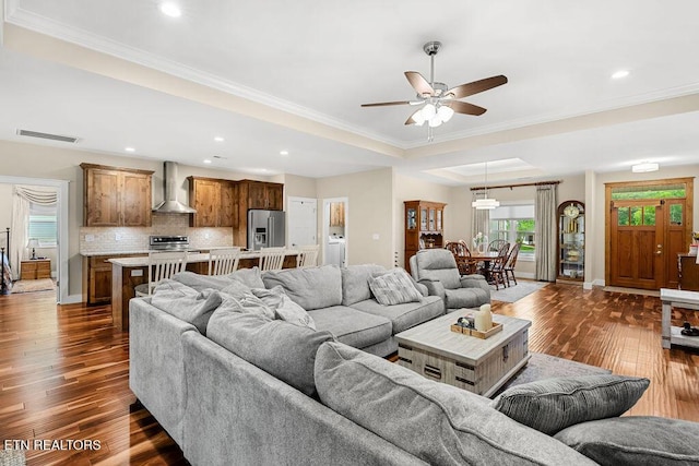 living room featuring dark wood-style flooring, ornamental molding, ceiling fan, a raised ceiling, and recessed lighting