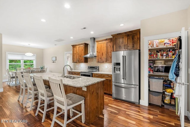 kitchen with appliances with stainless steel finishes, a sink, wall chimney exhaust hood, wood finished floors, and recessed lighting