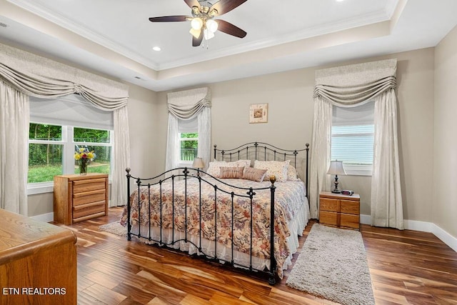 bedroom featuring a tray ceiling, crown molding, wood finished floors, baseboards, and recessed lighting