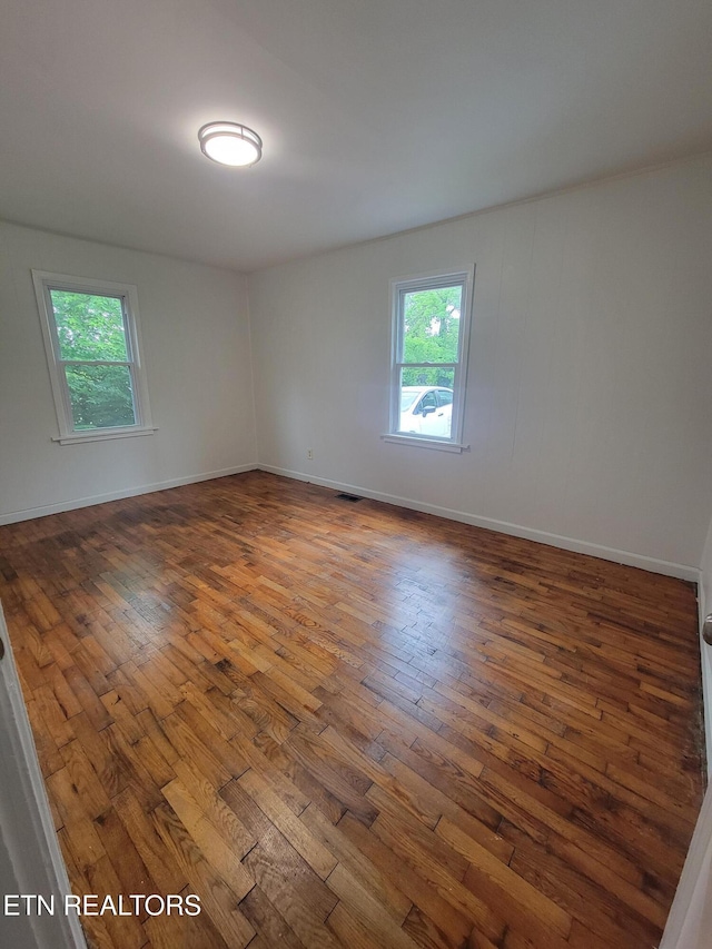 empty room featuring plenty of natural light, hardwood / wood-style flooring, and baseboards