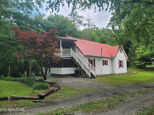view of front of property with stairs, a front yard, metal roof, and a sunroom