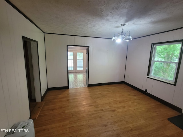 unfurnished room featuring wood finished floors, a chandelier, healthy amount of natural light, a textured ceiling, and baseboards