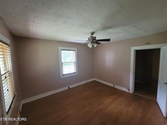 empty room with a textured ceiling, dark wood-type flooring, a ceiling fan, and baseboards