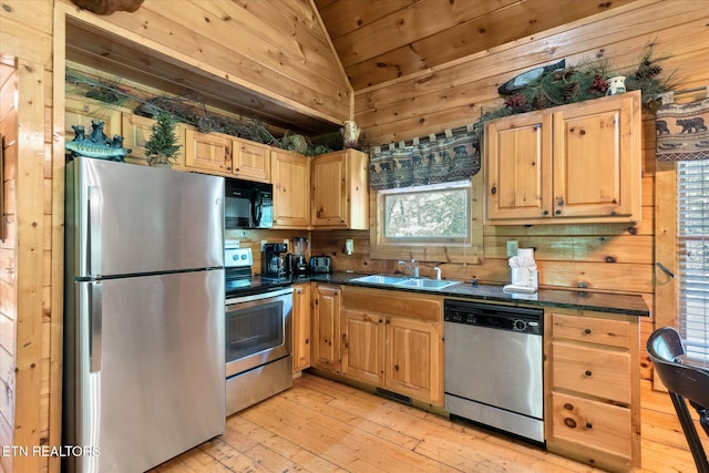 kitchen with appliances with stainless steel finishes, a sink, vaulted ceiling, dark countertops, and light wood-type flooring