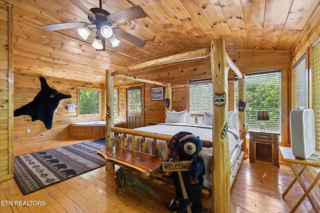 bedroom with vaulted ceiling, wooden walls, wood ceiling, multiple windows, and wood-type flooring