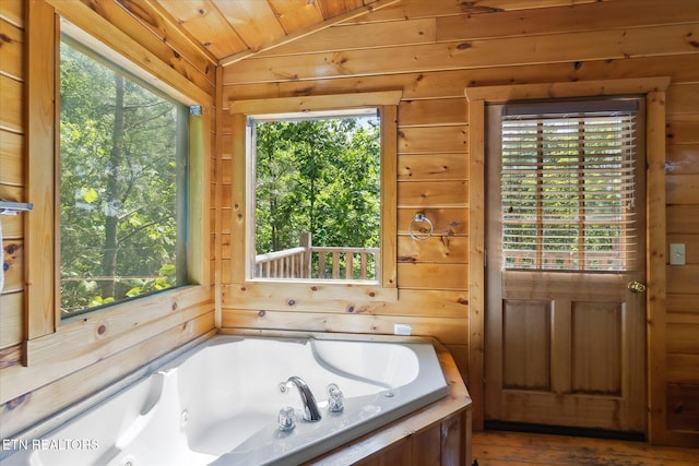 full bathroom with vaulted ceiling, plenty of natural light, a whirlpool tub, and wooden walls
