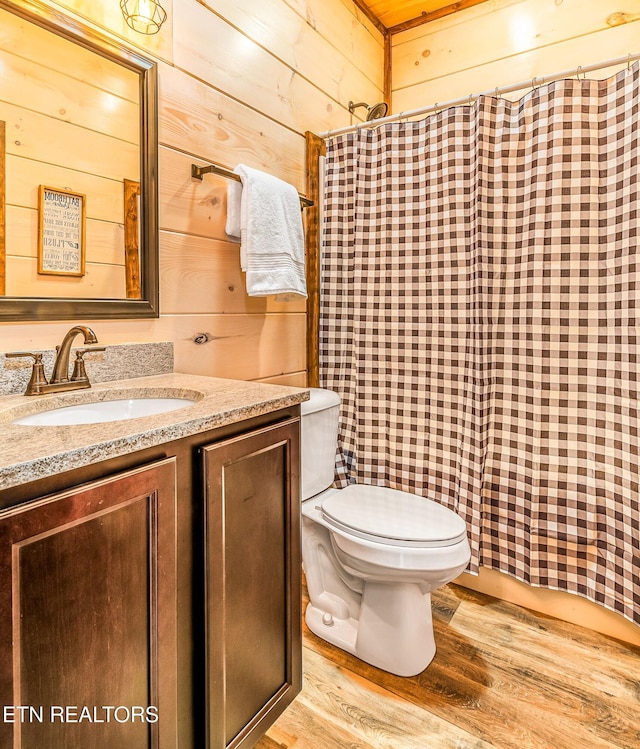 bathroom with toilet, wood finished floors, vanity, and wood walls