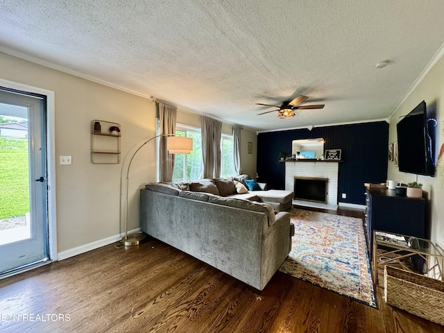 living room featuring a textured ceiling, dark wood-style flooring, crown molding, ceiling fan, and a brick fireplace
