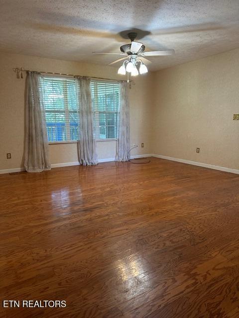 spare room featuring wood finished floors, a textured ceiling, ceiling fan, and baseboards