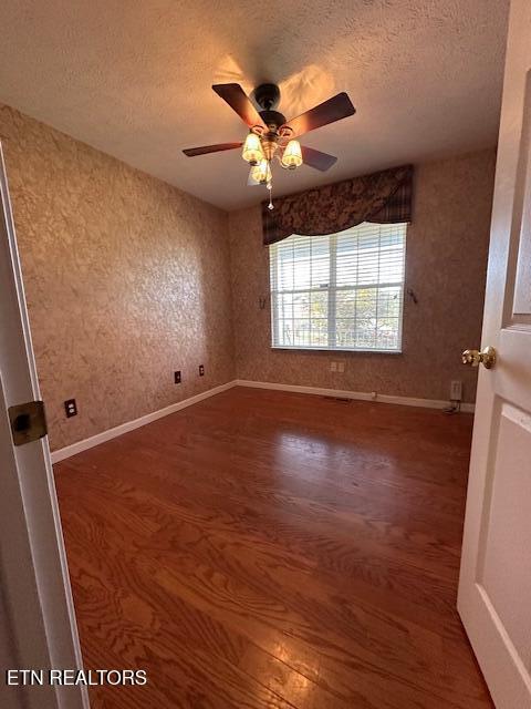 spare room with wood finished floors, a textured ceiling, a ceiling fan, and baseboards
