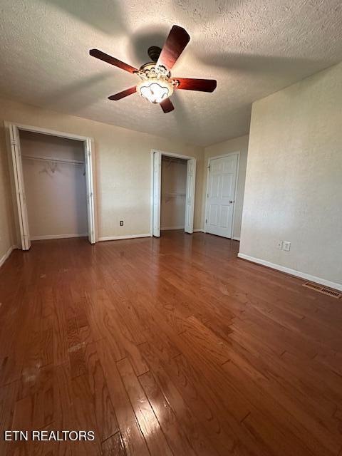 unfurnished bedroom with wood finished floors, two closets, a textured ceiling, baseboards, and ceiling fan