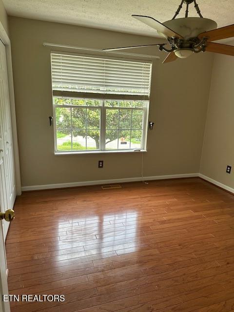unfurnished room with plenty of natural light, wood finished floors, baseboards, ceiling fan, and a textured ceiling