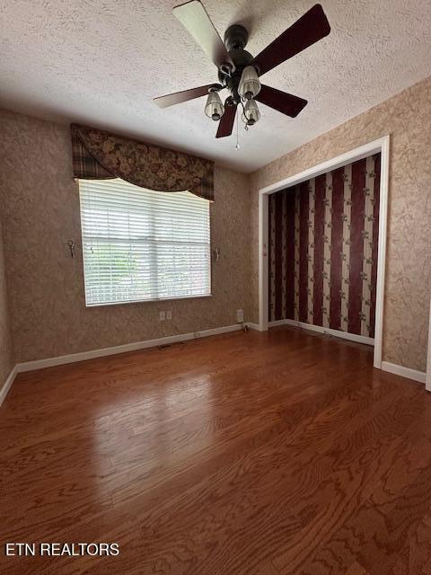 spare room featuring a textured ceiling, wood finished floors, a ceiling fan, and baseboards