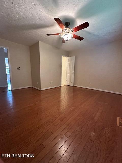 empty room featuring baseboards, dark wood-type flooring, a ceiling fan, and a textured ceiling