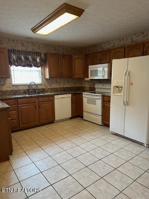 kitchen featuring white appliances, a sink, dark countertops, brown cabinetry, and a textured ceiling