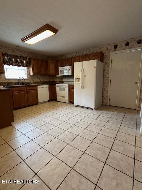 kitchen featuring white appliances, wallpapered walls, a sink, dark countertops, and light tile patterned floors