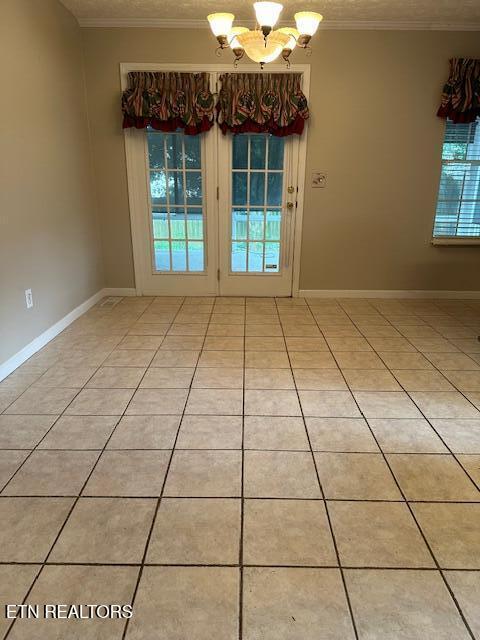 spare room with a chandelier, ornamental molding, light tile patterned floors, and baseboards