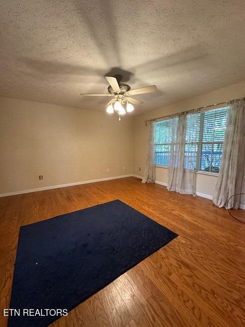 empty room featuring a ceiling fan, a textured ceiling, baseboards, and wood finished floors