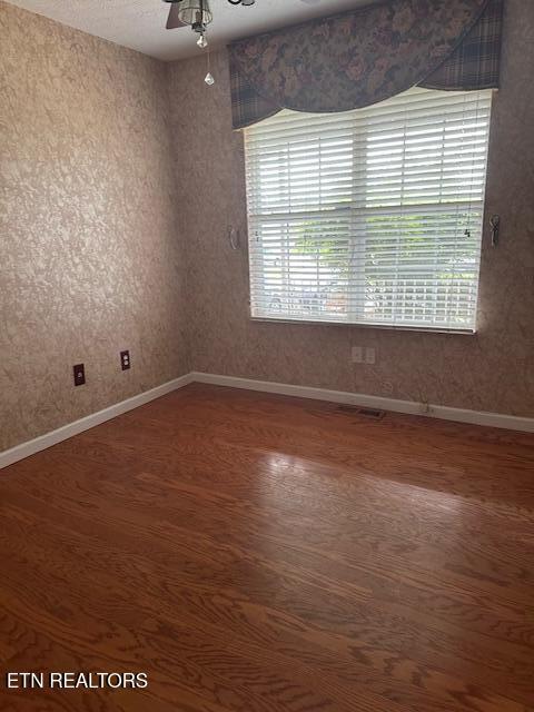unfurnished room featuring wood finished floors, baseboards, and a ceiling fan