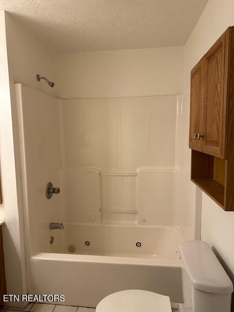 full bath with toilet, a textured ceiling, shower / bath combination, and tile patterned floors