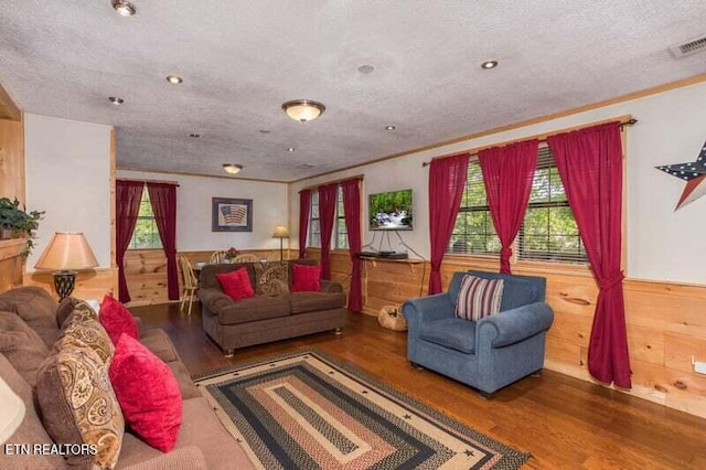 living room featuring wood finished floors, a wainscoted wall, wooden walls, a textured ceiling, and crown molding
