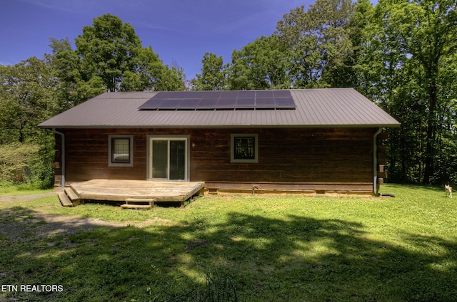rear view of property featuring a yard, roof mounted solar panels, a wooden deck, and metal roof