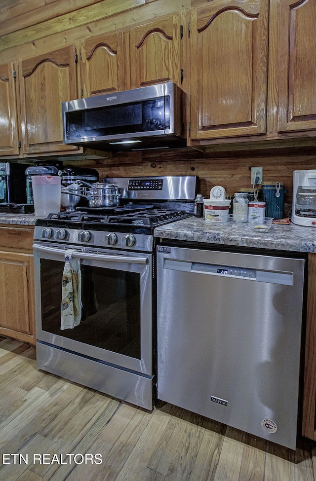 kitchen with stainless steel appliances, brown cabinetry, and light wood finished floors