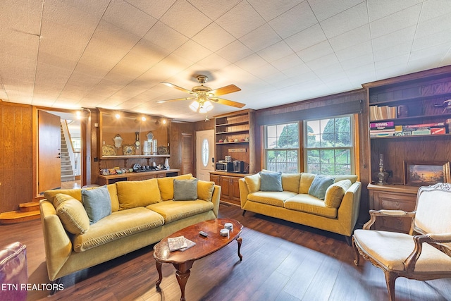 living area with wood walls, hardwood / wood-style floors, ceiling fan, and built in shelves
