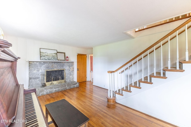 unfurnished living room with a stone fireplace, stairs, and wood finished floors