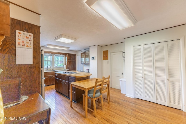 kitchen with butcher block countertops, light wood finished floors, a sink, dark brown cabinets, and stovetop