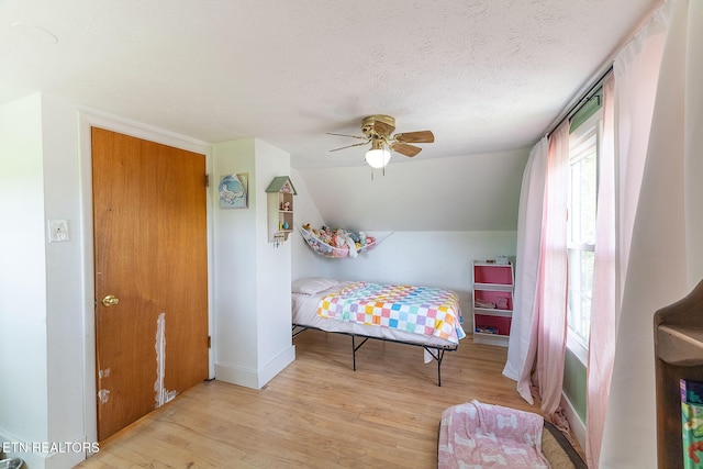 bedroom featuring light wood-style flooring, vaulted ceiling, baseboards, a textured ceiling, and a ceiling fan