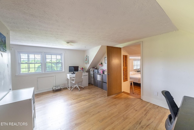 office featuring a textured ceiling, light wood-style flooring, baseboards, and vaulted ceiling