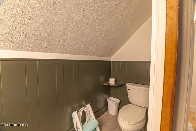 bathroom featuring lofted ceiling, a textured ceiling, toilet, a wainscoted wall, and wood finished floors