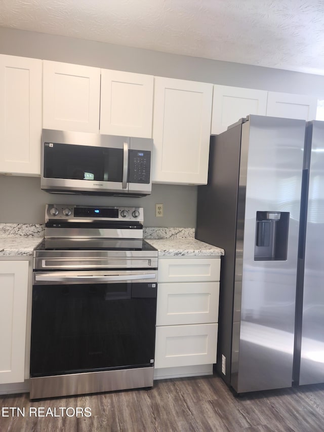 kitchen featuring stainless steel appliances, white cabinets, dark wood finished floors, and light stone counters