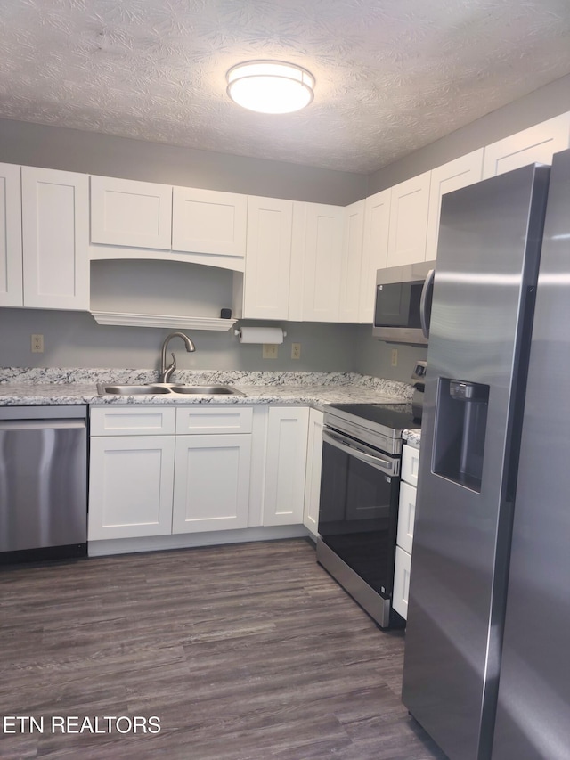 kitchen featuring stainless steel appliances, a sink, white cabinets, a textured ceiling, and dark wood finished floors