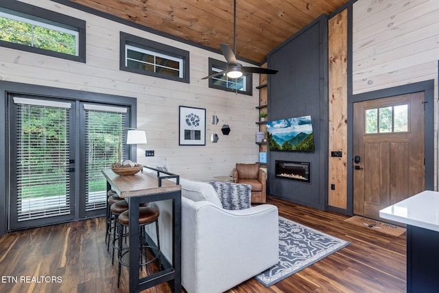 living area featuring wooden walls, wooden ceiling, vaulted ceiling, a glass covered fireplace, and a ceiling fan