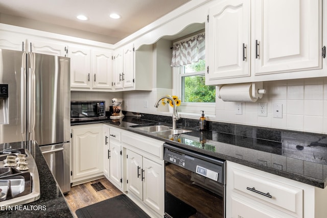 kitchen featuring appliances with stainless steel finishes, a sink, white cabinetry, light wood-type flooring, and dark stone countertops