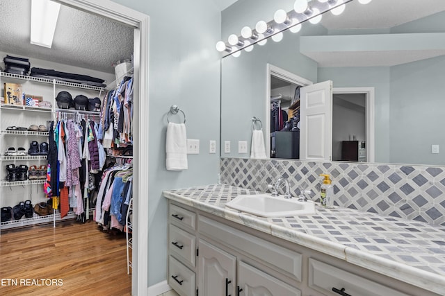 bathroom featuring tasteful backsplash, wood finished floors, a walk in closet, and vanity