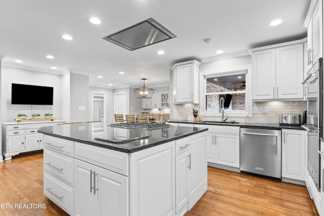 kitchen with stainless steel appliances, a sink, ornamental molding, white cabinets, and a center island