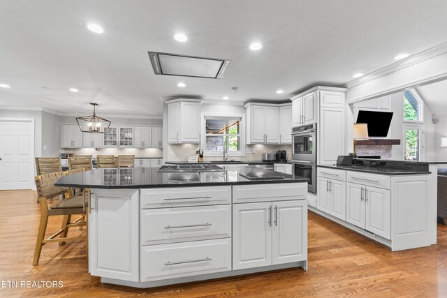 kitchen with ornamental molding, a sink, a kitchen island, white cabinets, and appliances with stainless steel finishes