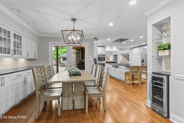 dining area featuring beverage cooler, light wood-style flooring, a chandelier, ornamental molding, and recessed lighting