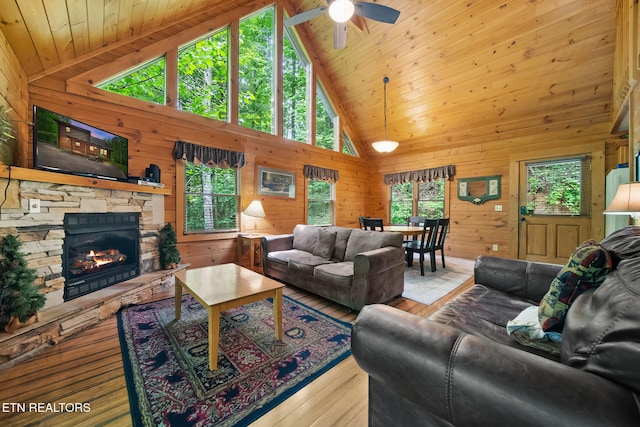 living area featuring wood walls, ceiling fan, a fireplace, high vaulted ceiling, and hardwood / wood-style floors