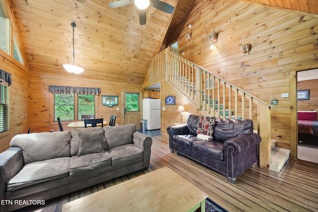 living room with wood walls, wood-type flooring, stairs, wooden ceiling, and high vaulted ceiling