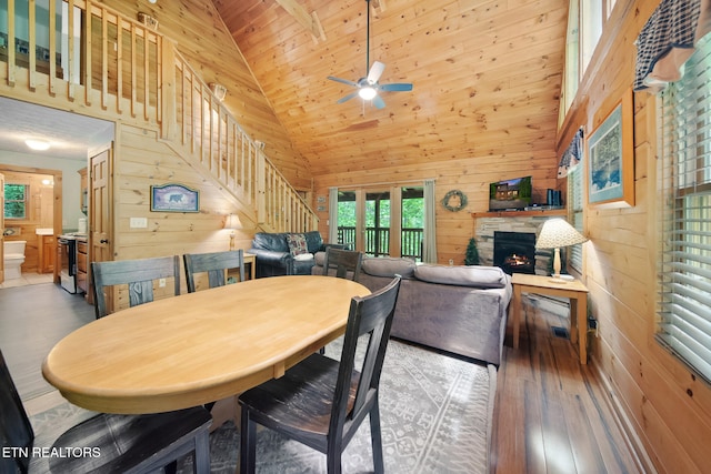 dining area with wooden walls, hardwood / wood-style floors, stairs, a fireplace, and ceiling fan
