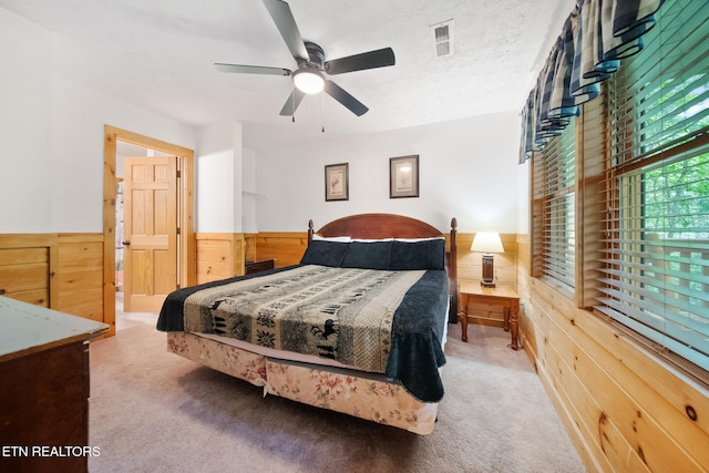 carpeted bedroom with wainscoting, wooden walls, and ceiling fan