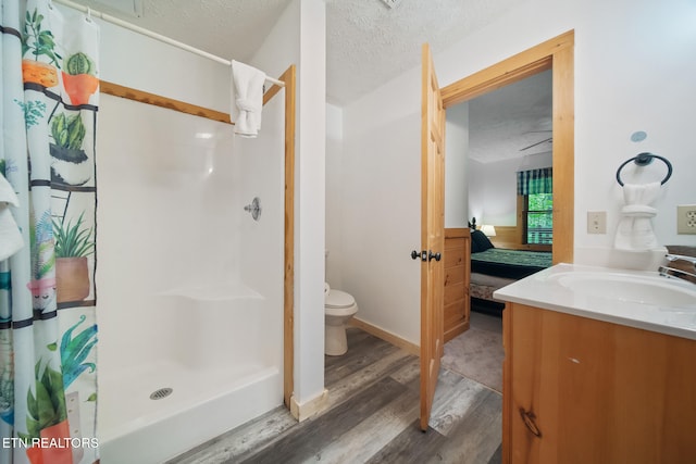 ensuite bathroom featuring a shower stall, wood finished floors, a textured ceiling, toilet, and vanity