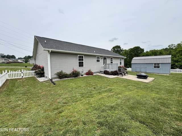rear view of property with a fire pit, an outdoor structure, a deck, and roof with shingles