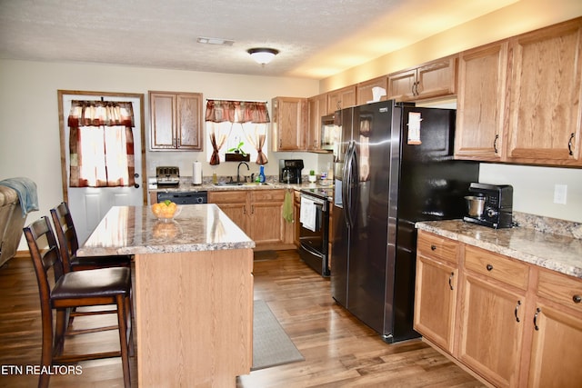 kitchen featuring black appliances, a breakfast bar area, light wood-type flooring, light stone countertops, and a kitchen island