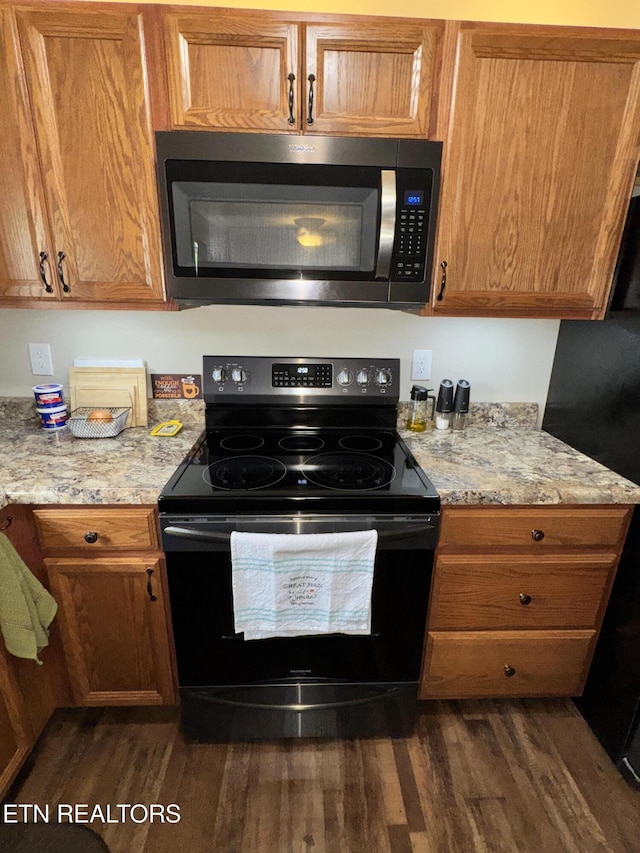 kitchen with black electric range oven, dark wood finished floors, brown cabinets, and light stone counters