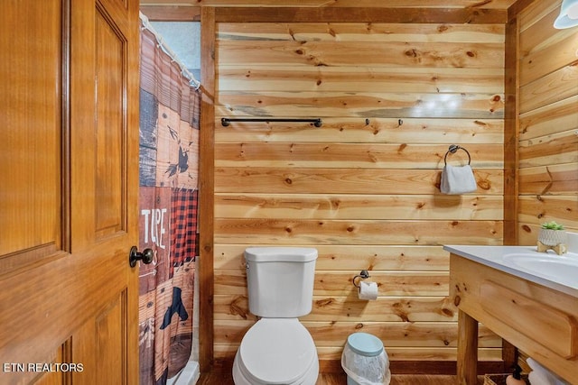 bathroom with wooden walls, toilet, vanity, and a shower with shower curtain